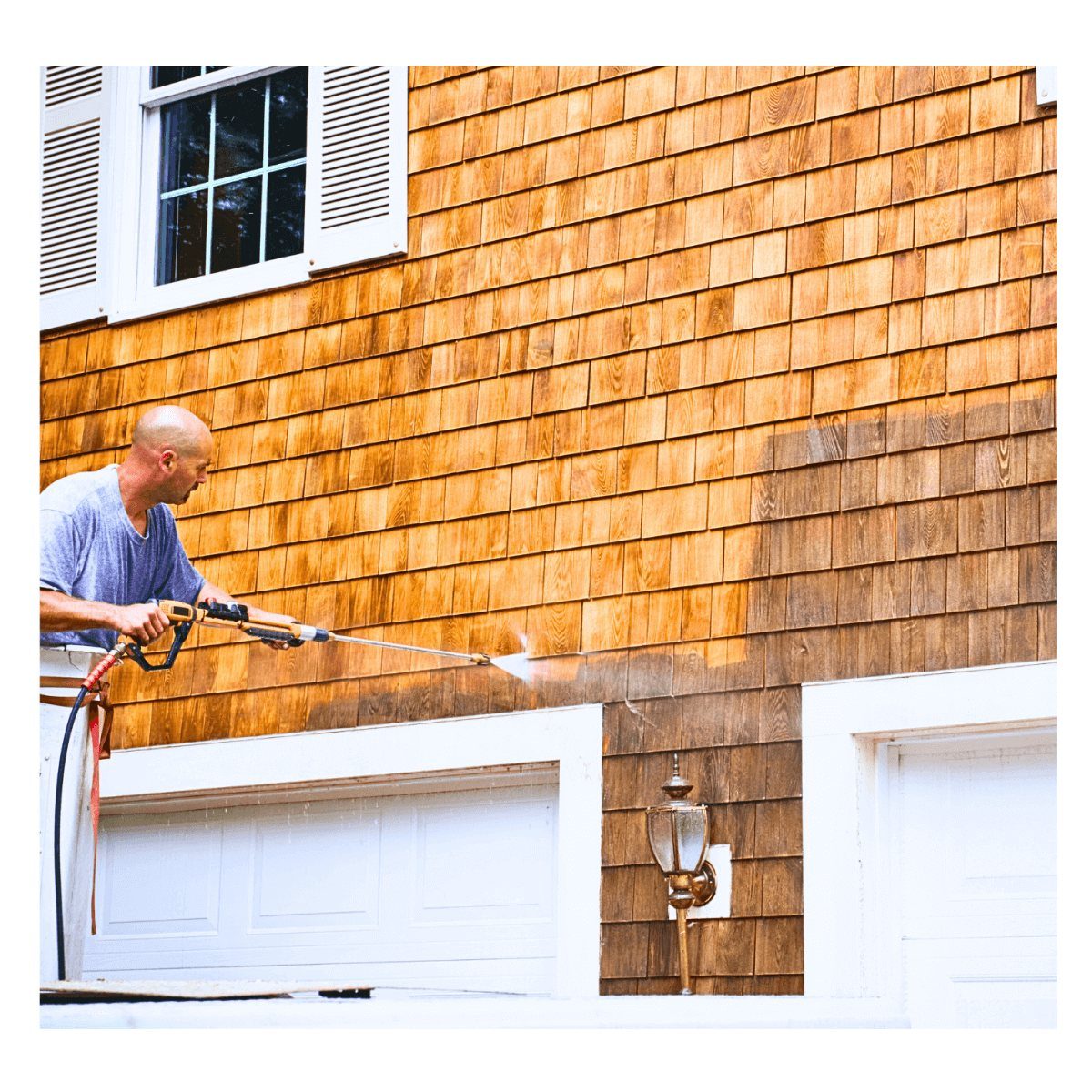 Crew member soft washing cedar shake siding, the cleaned half bright against the untreated half